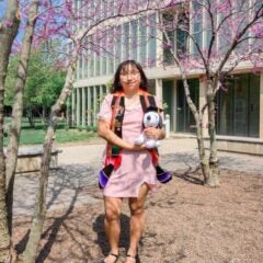 Ana Martinez smiling standing underneath tree with purple flowers in front of glass window building