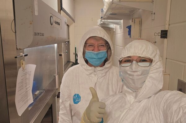 Researchers in cleanroom wearing cleanroom suits giving thumbs up