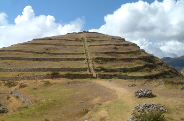 Terraced pyramidal monument covered in grass on a sunny day with bright fluffy clouds in the background