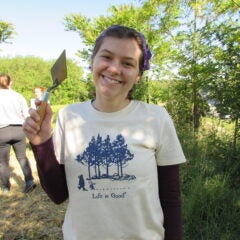 Ava standing outdoors and holding up a trowel