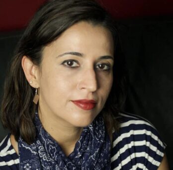 Dr. Bedi - wearing a striped shirt, a neck scarf, and earrings.
                  